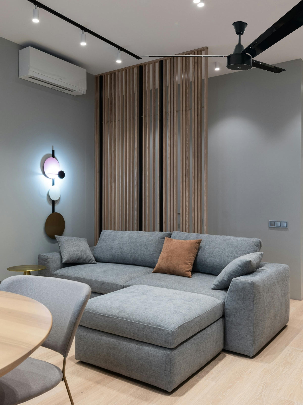 Modern lounge interior featuring a slimline inverter split AC and a 1.65m black ceiling fan above a grey sectional sofa.